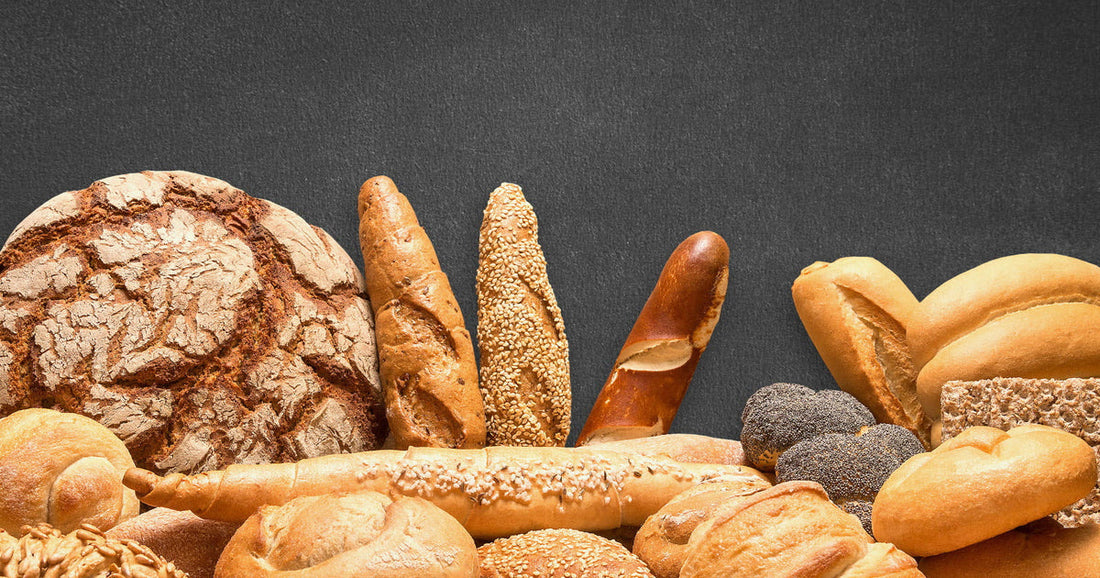 Assortimento di pagnotte, baguette e panini appena sfornati su fondo chiaro